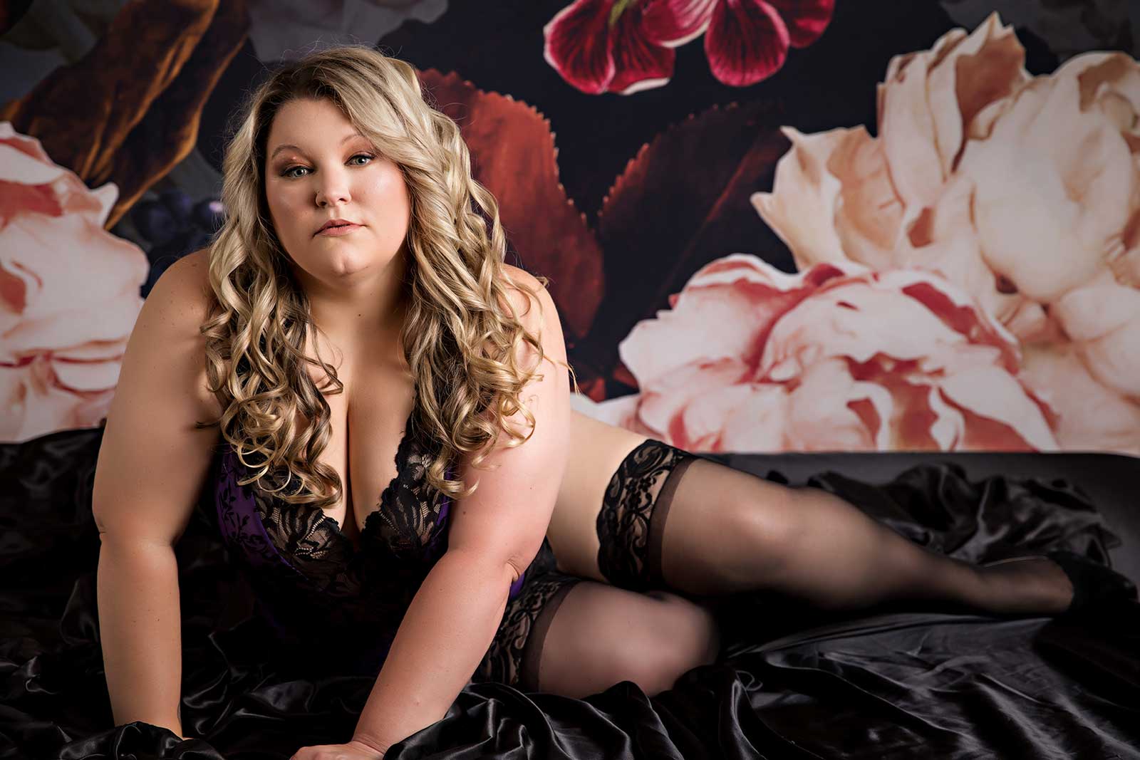 Woman sitting on black silk sheets with floral background boudoir session