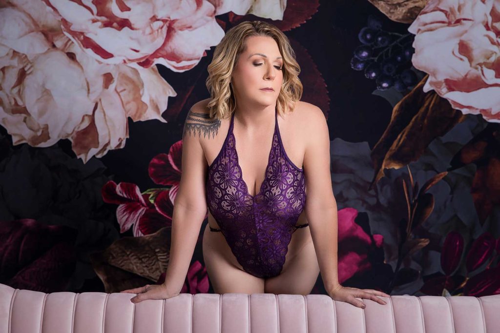 Woman in purple lingerie standing posing in front of floral backdrop
